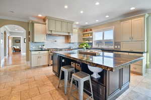 Kitchen featuring a kitchen island, dark stone counters, a breakfast bar, tasteful backsplash, and light tile floors