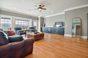 Living room with ornamental molding, ceiling fan, ice maker, and light hardwood / wood-style flooring