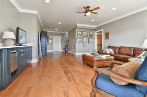 Living room with light hardwood / wood-style floors, ornamental molding, and ceiling fan