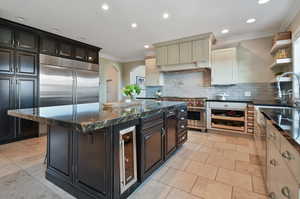 Kitchen featuring high quality appliances, a kitchen island, dark stone counters, tasteful backsplash, and light tile floors