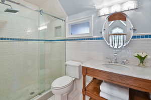 Bathroom with walk in shower, tile floors, tile walls, vanity, and toilet