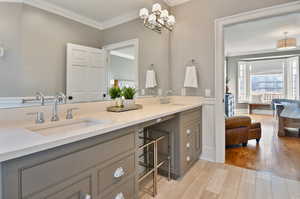 Bathroom with ornamental molding, an inviting chandelier, double vanity, and wood-type flooring