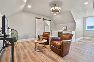 Living area featuring vaulted ceiling, a barn door, light hardwood / wood-style floors, and beverage cooler