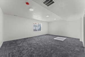 Empty room featuring a textured ceiling and dark colored carpet