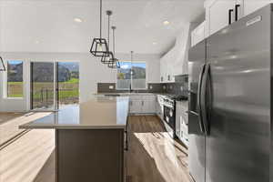 Kitchen with hanging light fixtures, stainless steel appliances, white cabinets, backsplash, and wood-type flooring