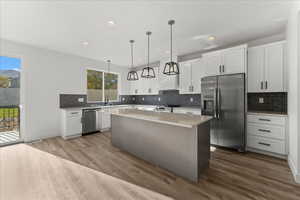 Kitchen featuring pendant lighting, backsplash, a center island, hardwood / wood-style flooring, and appliances with stainless steel finishes