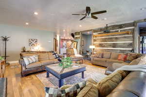 Living room featuring hardwood / wood-style floors, wooden walls, ceiling fan, and a textured ceiling