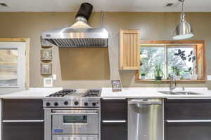 Kitchen featuring appliances with stainless steel finishes, light stone counters, dark brown cabinetry, pendant lighting, and sink