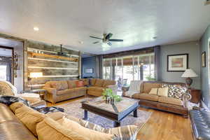 Living room with wooden walls, ceiling fan, a textured ceiling, and light wood-type flooring