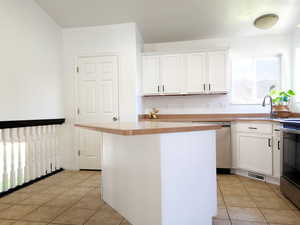 Kitchen with appliances with stainless steel finishes, white cabinetry, light tile floors, and a kitchen island