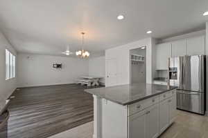 Kitchen featuring a center island, white cabinetry, stainless steel fridge with ice dispenser, decorative light fixtures, and wood-type flooring