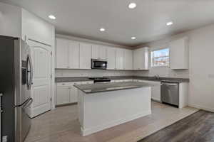 Kitchen with a center island, dark stone countertops, stainless steel appliances, white cabinets, and sink