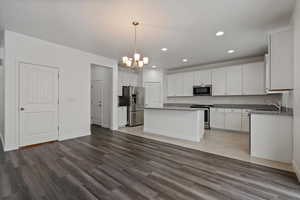 Kitchen featuring tile flooring, decorative light fixtures, a kitchen island, white cabinets, and appliances with stainless steel finishes