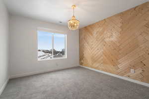 Carpeted empty room featuring a notable chandelier and wood walls