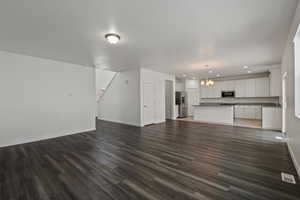 Unfurnished living room with dark hardwood / wood-style floors, a notable chandelier, and sink