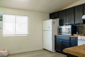 Kitchen with white appliances, light hardwood / wood-style floors, and vaulted ceiling