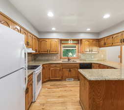 Kitchen with light wood-type flooring, white appliances, light stone counters, backsplash, and sink