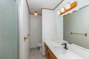 Bathroom featuring hardwood / wood-style floors, crown molding, a textured ceiling, toilet, and vanity