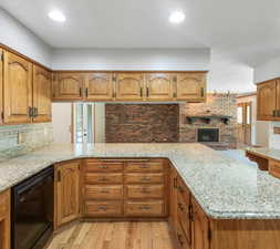 Kitchen featuring light stone counters, light hardwood / wood-style floors, dishwasher, and a fireplace