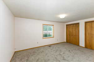 Unfurnished bedroom with light carpet, multiple closets, and a textured ceiling