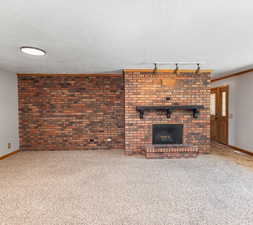 Unfurnished living room with carpet floors, track lighting, a brick fireplace, and brick wall