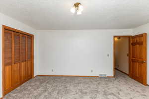 Unfurnished bedroom with light carpet, a closet, and a textured ceiling