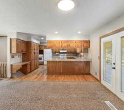 Kitchen with kitchen peninsula, light carpet, sink, white appliances, and a textured ceiling