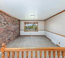 Carpeted empty room featuring a textured ceiling, brick wall, and ornamental molding