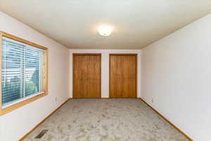 Unfurnished bedroom featuring two closets, light carpet, and a textured ceiling