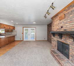 Living room with french doors, a fireplace, a textured ceiling, light carpet, and rail lighting