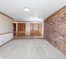 Carpeted empty room with a textured ceiling, brick wall, and ornamental molding