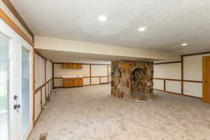 Basement with a stone fireplace, a textured ceiling, and light carpet