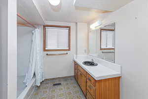 Bathroom featuring shower / bath combo with shower curtain, vanity, a textured ceiling, and tile patterned flooring