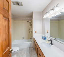 Full bathroom with tiled shower / bath, a textured ceiling, hardwood / wood-style flooring, toilet, and large vanity