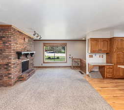 Unfurnished living room featuring track lighting, a textured ceiling, light hardwood / wood-style flooring, and a brick fireplace