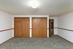 Unfurnished bedroom featuring multiple closets, a textured ceiling, and light colored carpet