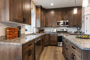 Kitchen with sink, light stone countertops, light wood-type flooring, and stainless steel appliances