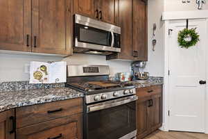 Kitchen featuring stainless steel appliances, dark brown cabinetry, dark stone counters, and light wood-type flooring