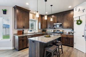 Kitchen with stainless steel appliances, light stone counters, a wealth of natural light, and light hardwood / wood-style flooring