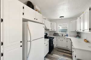 Kitchen with dark hardwood / wood-style floors, white fridge, black / electric stove, a textured ceiling, and white cabinets