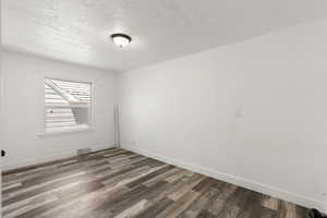 Empty room with a textured ceiling and dark wood-type flooring