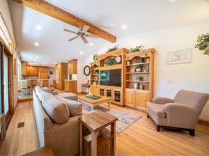 Living room with ceiling fan, lofted ceiling with beams, and light wood-type flooring