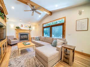 Living room with ceiling fan, lofted ceiling with beams, and light hardwood / wood-style floors