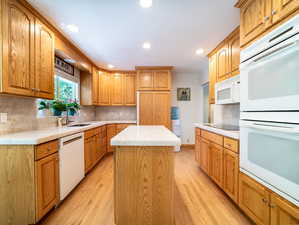 Kitchen featuring a kitchen island, tasteful backsplash, light wood-type flooring, sink, and white appliances