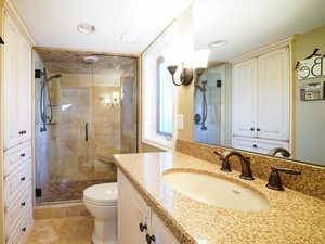 Bathroom with tile floors, a shower with door, vanity with extensive cabinet space, and toilet