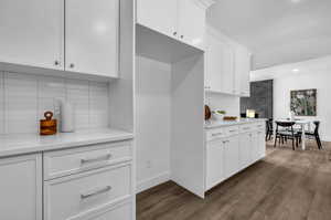 Kitchen with dark hardwood / wood-style floors, light stone counters, white cabinets, and tasteful backsplash