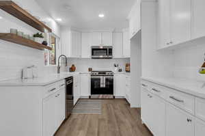 Kitchen featuring light hardwood / wood-style flooring, stainless steel appliances, tasteful backsplash, light stone countertops, and white cabinets