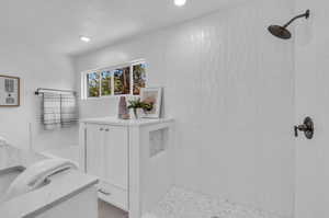 Bathroom featuring tiled shower and vanity