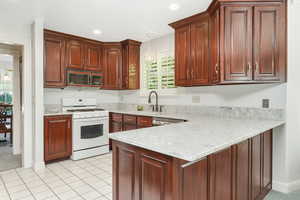 Barlow's custom cherry cabinet kitchen with kitchen quartz peninsula, gas range gas stove, dishwasher, light tile floors, and sink