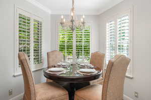 Dining space featuring plenty of natural light, an inviting chandelier, and crown molding and plantation shutters overlooking the  "secret garden"